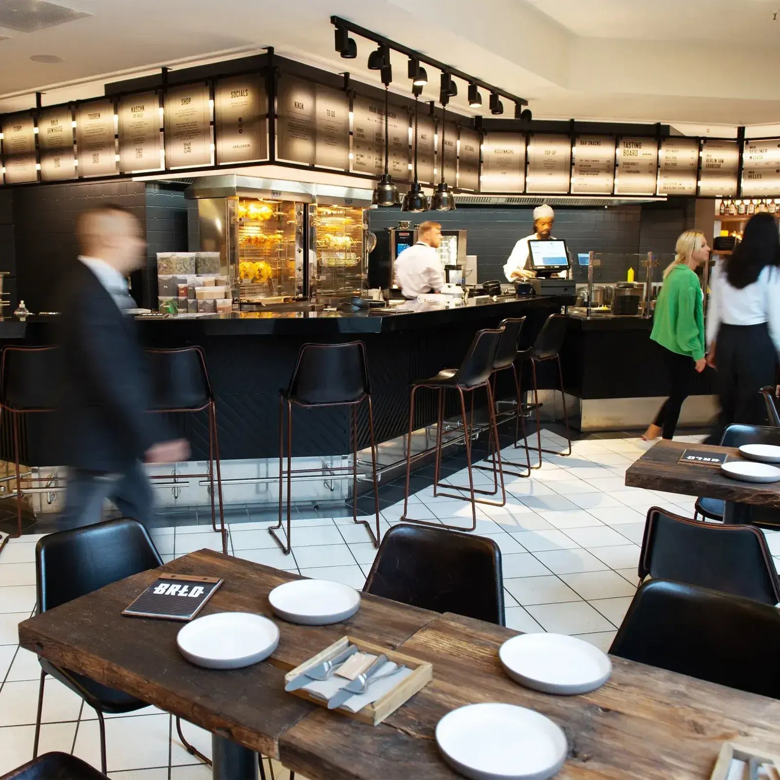 Belebte Restaurantszene in einem Restaurant von BRLO. Eine schwarze Bar mit weißen Bodenfliesen.