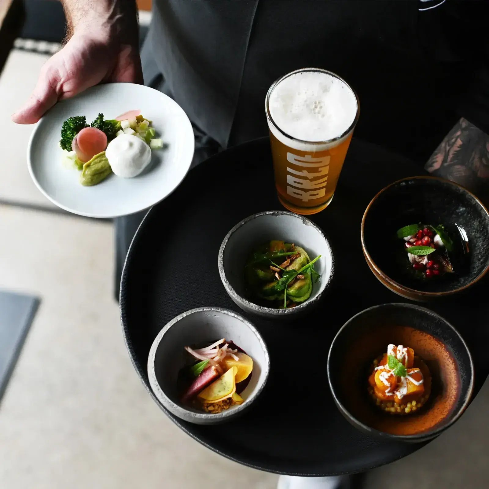 Ein von oben fotografiertes Tablett mit Tapas und einem Bier von BRLO, gehalten von einem Kellner