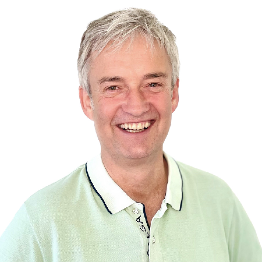 Ein lächelnder Mann mit grauen, kurzen Haaren und einem hellgrünen Oberteil.