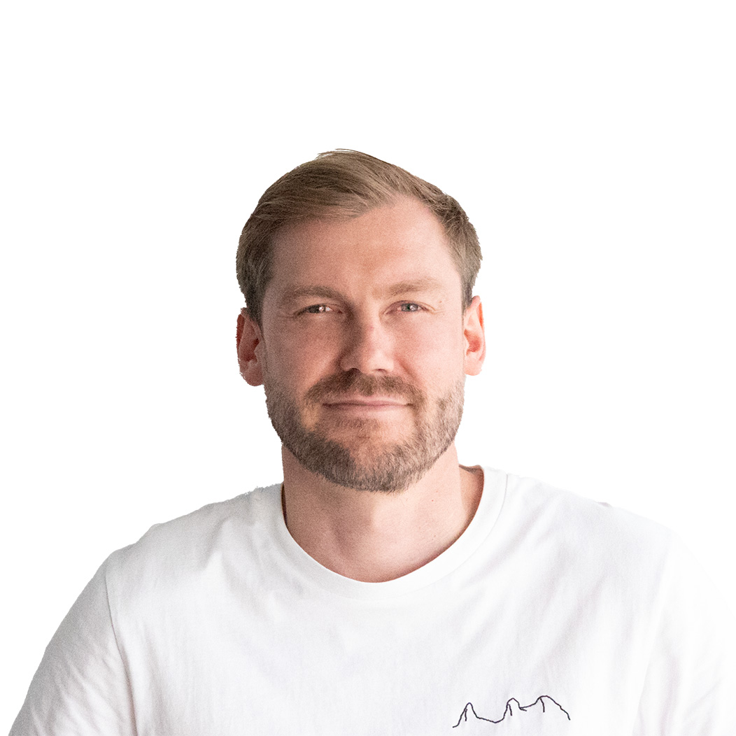 Ein junger Mann mit blonden, kurzen Haaren, einem skeptischen Blick, einem Drei-Tage-Bart und einem weißen Oberteil.