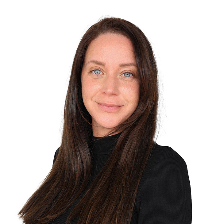 Eine lächelnde junge Frau mit blauen Augen,  dunkelbraunen, langen Haaren und einem schwarzen Pullover.