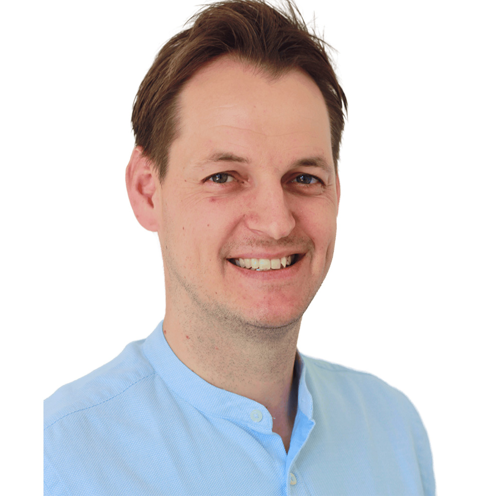 Ein lächelnder Mann mit dunkelbraunen Haaren und einem  hellblauen Oberteil.