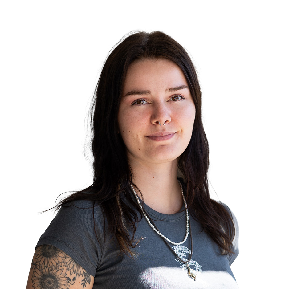Eine lächelnde, junge Frau mit dunklen, schulterlangen Haaren, einem Nasenpiercing, einer Silberkette und einem dunkelblauen und weißen T-Shirt.