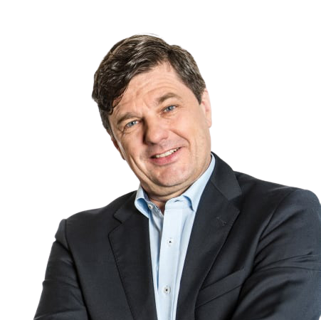Ein lächelnder Mann mit dunkelbraunen Haaren, einem hellblauen Hemd und darüber einem schwarzen Jacket.