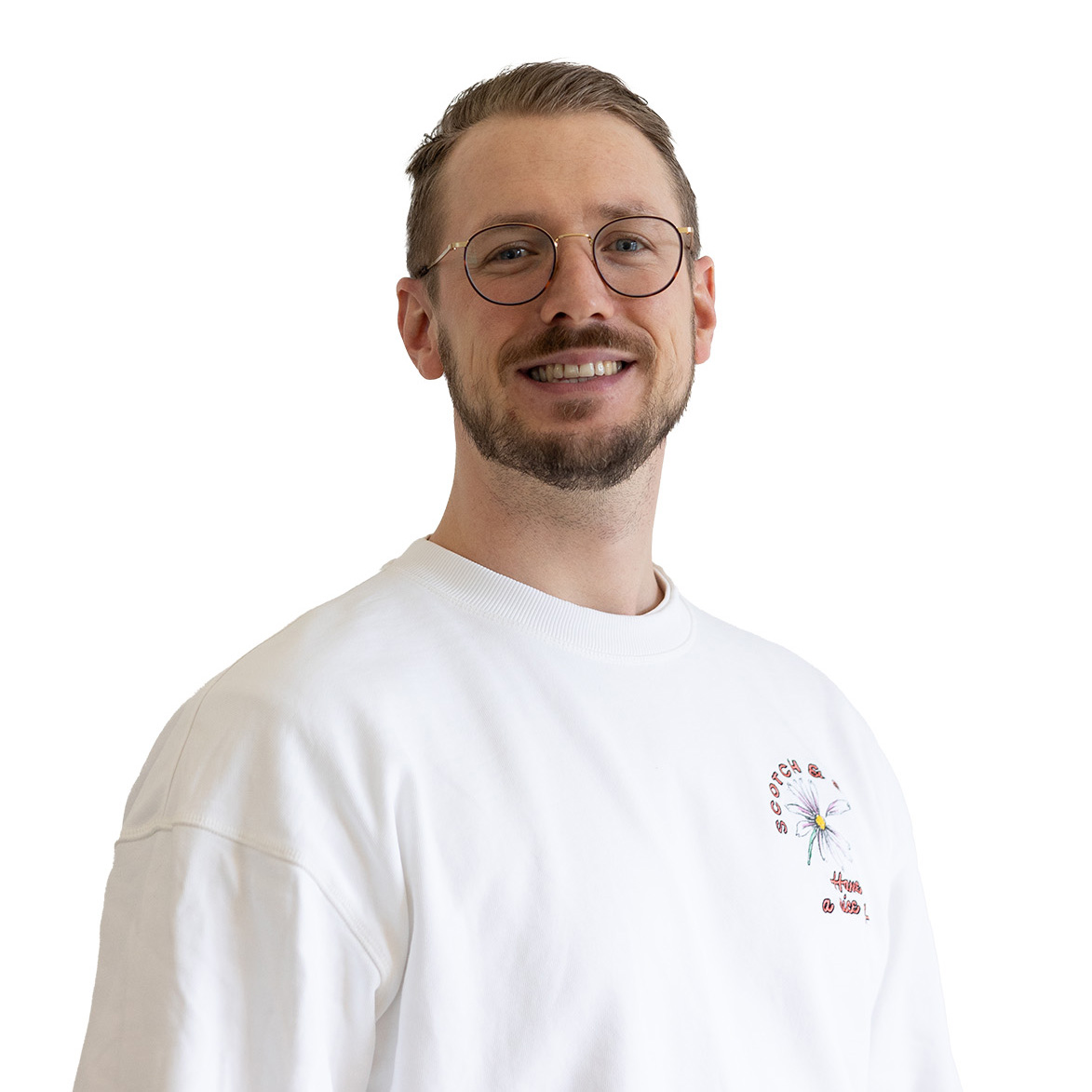 Ein lächelnder, junger Mann mit dunkelblonden Haaren, einem dunkelblonden Bart und einem weißen T-Shirt.