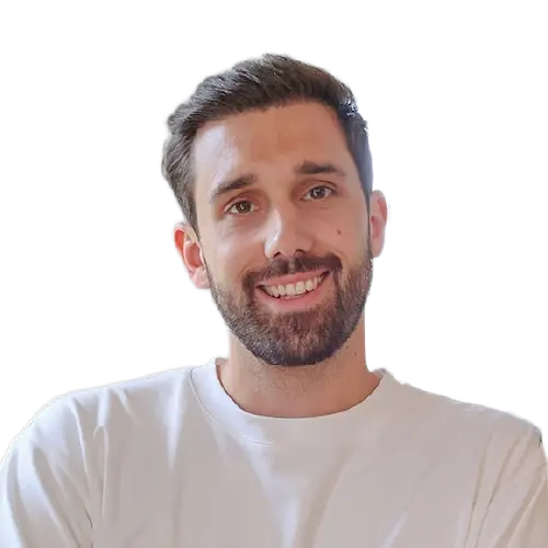 Ein lächelnder junger Mann mit dunkelbraunen, kurzen Haaren und einem weißen Oberteil.