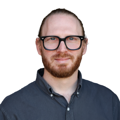 Ein lächelnder, junger Mann mit blonden, zusammmengebundenen Haaren, einem dunkelblonden Bart und einem blauen Oberteil.