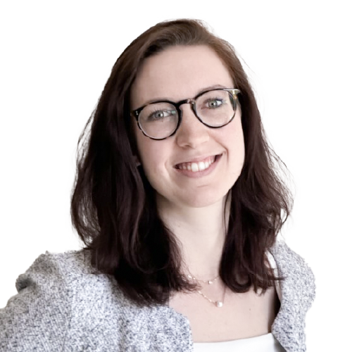 Eine lächelnde Frau mit hellbraunen Haaren, einer Brille und einer grauen Jacke.