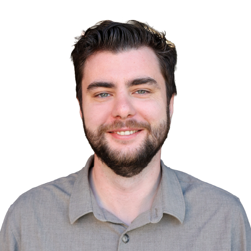 Ein lächelnder, junger Mann mit kurzen, braunen Haare, einem dunkelbraunen Bart und einem grauen Oberteil.